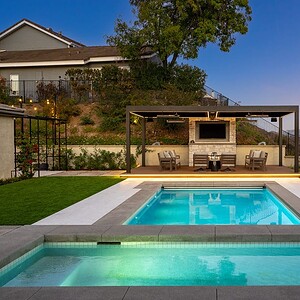 The outdoor pool area, complete with lounge chairs, offers a covered seating space overlooking the enchanting Sunset Trails against a hilly landscape at dusk.