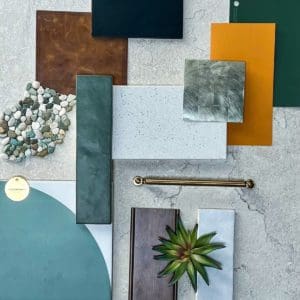 A flat lay display of various material samples, including Eichler Orange tiles, color swatches, pebbles, a brass handle, and a small succulent plant, arranged on a stone surface.