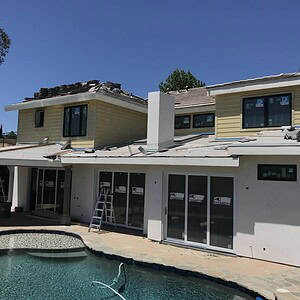 A two-story house under construction, with partial roofing and exterior work incomplete, promises modern refreshment. A ladder leans against the house, and an in-ground pool is in the foreground.