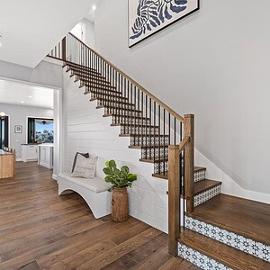 A modern foyer with wooden flooring, a staircase with metal railings, a white bench, a potted plant, and zebra artwork on the wall welcomes you. The room opens to the Carrita Seaview dining area, offering an exquisite vista.