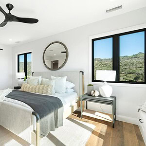 A modern bedroom with a neatly made bed, dark framed windows, and a round mirror showcases elegance. A door slides open to reveal a bathroom. The room is well-lit by natural light, offering a serene Carrita Seaview ambiance.