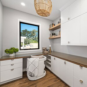 A modern, well-lit home office with a large window offering a Carrita Seaview, white cabinets, wooden countertops, a chair with a blanket, and a few plants and decorative items on the shelves and countertop.