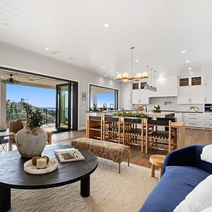 Modern open-concept living room with large sliding glass doors leading to a balcony with hillside views. Includes a cozy seating area, a dining table, and a kitchen island with chairs—offering the perfect blend of comfort and style in the picturesque Carrita Seaview.