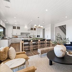 A modern open-concept living area with a white kitchen, dining table with wooden chairs, and a navy blue sofa around a black coffee table. The Carrita Seaview room features large windows and light wood flooring.