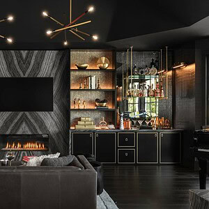 A modern living room exudes sophisticated glamour with a fireplace, wall-mounted TV, built-in shelves adorned with decorative items, a bar area, and stylish lighting fixtures. The dark interior color scheme complements the luxurious furnishings beautifully.