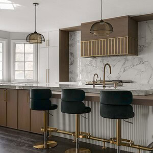 Modern kitchen with marble countertops, an island with dark green velvet bar stools, brass fixtures, white and wood cabinetry, pendant lights, and large windows providing natural light. This space exudes sophisticated glamour at every turn.