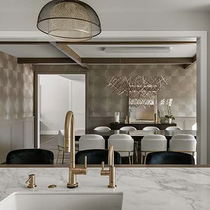 Modern kitchen and dining area exuding sophisticated glamour, featuring a marble countertop with a gold faucet, a large wooden cabinet, and a dining table with white chairs accompanied by a decorative geometric art piece on the wall.