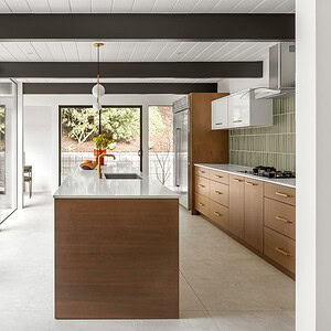 Modern kitchen with a central island, wooden cabinets, stainless steel appliances, and large glass doors opening to a patio. The space features a minimalist design with clean lines, natural light, and a touch of Eichler Orange for a vibrant yet sophisticated feel.
