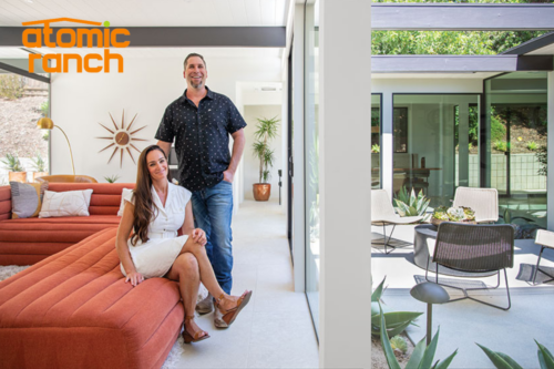 A man and woman pose in a modern, sunlit living room with large windows and outdoor seating visible outside. An Atomic Ranch logo graces the top-left corner, adding a touch of retro charm.
