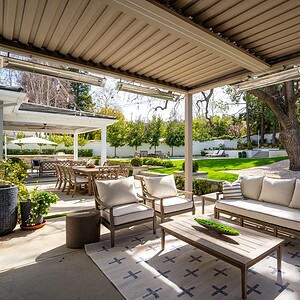 Outdoor patio with modern seating, overhead pergola, and a view of a manicured lawn and garden with large trees. Dining table and chairs are visible in the background, reminiscent of the serene beauty found in Westlake Trails.