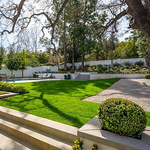 A backyard in Westlake Trails features a well-manicured lawn, a pool with lounge chairs, and various trees and shrubs. Steps lead down to different areas of the yard, creating a serene oasis perfect for relaxation.