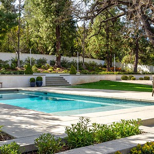 Nestled in the serene enclave of Westlake Trails, the outdoor swimming pool is surrounded by a patio with two lounge chairs and beautifully landscaped with various plants, trees, and shrubs in the background.