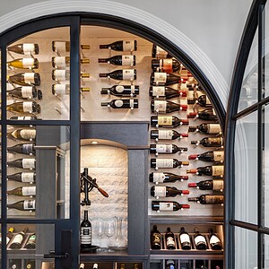 A wine cellar in Westlake Trails with floor-to-ceiling wine racks filled with bottles, a central countertop featuring wine accessories, and wooden crates below for additional bottle storage.
