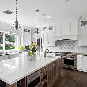 A modern kitchen in Westlake Trails featuring white cabinets, a large marble island, stainless steel appliances, pendant lights, and a window overlooking a garden.