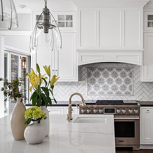 A modern kitchen with white cabinets, a patterned backsplash, stainless steel stove, and a countertop displaying flower vases, situated in the elegant Westlake Trails neighborhood.