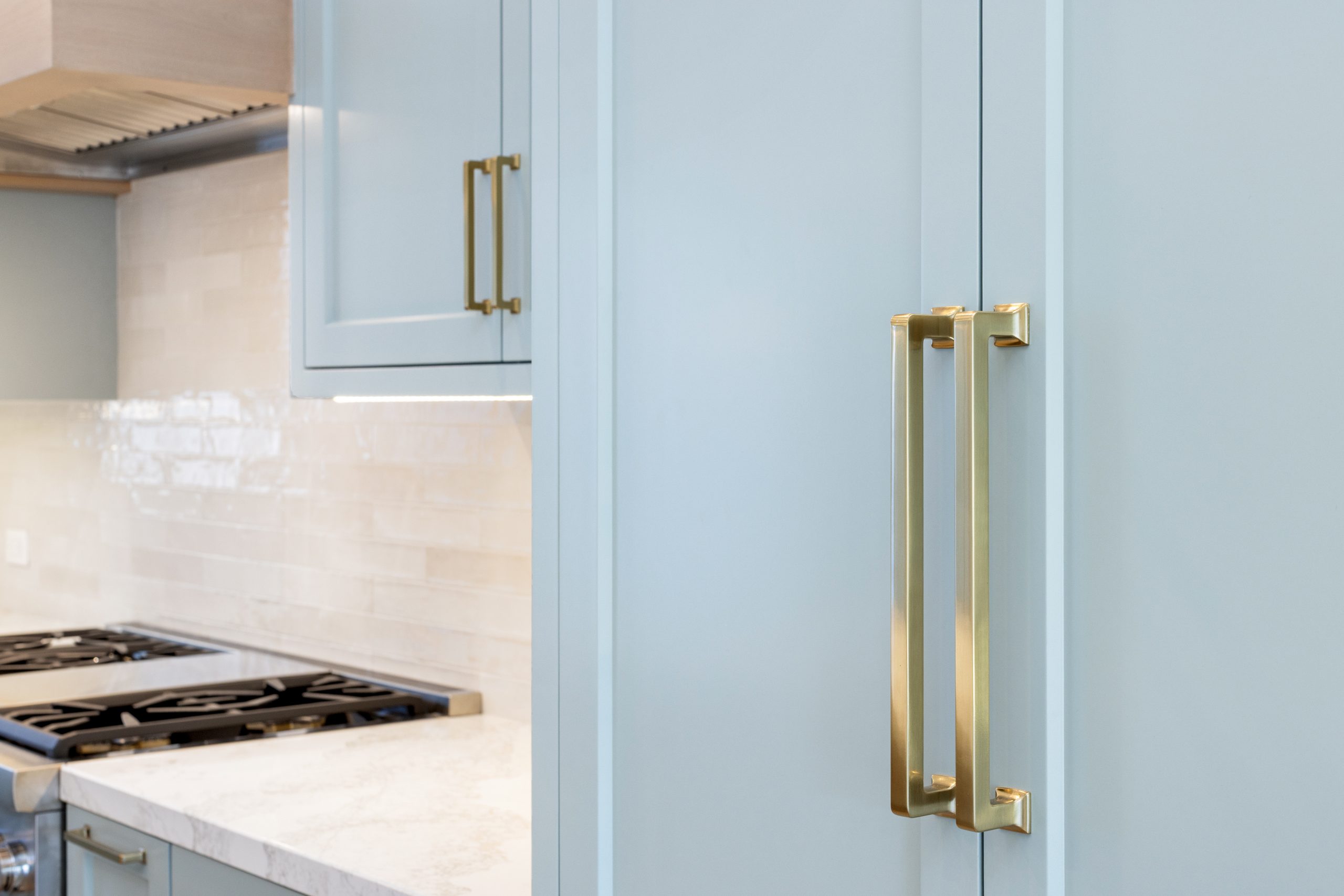 A coastal home reimagined kitchen with soft blue cabinets, and warm brass accents remodel by JRP Design and Remodel.