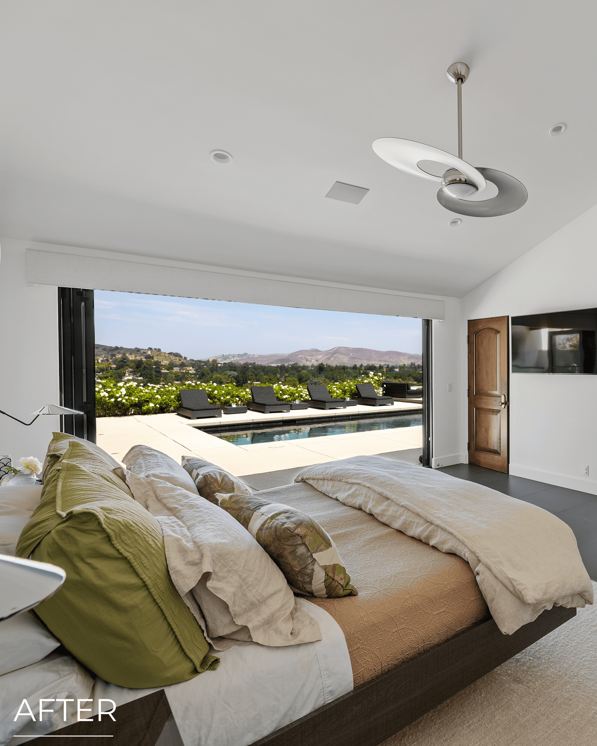 Spacious bedroom with large window overlooking pool and scenic landscape.