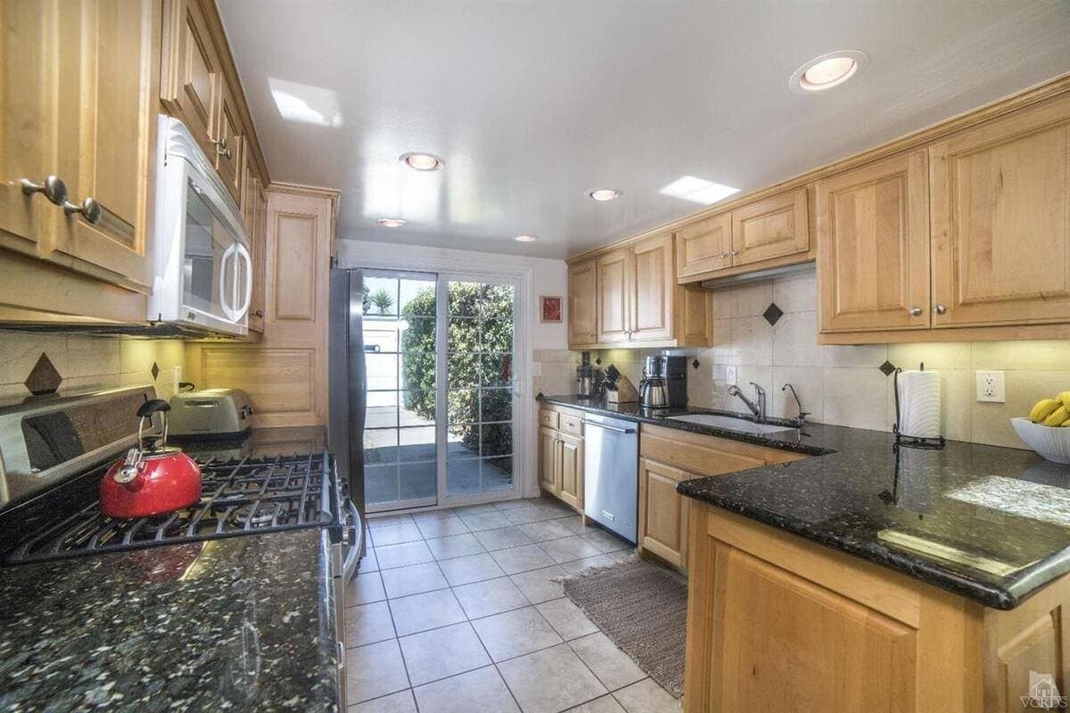 Bright coastal kitchen with natural wood cabinets and black granite countertops.