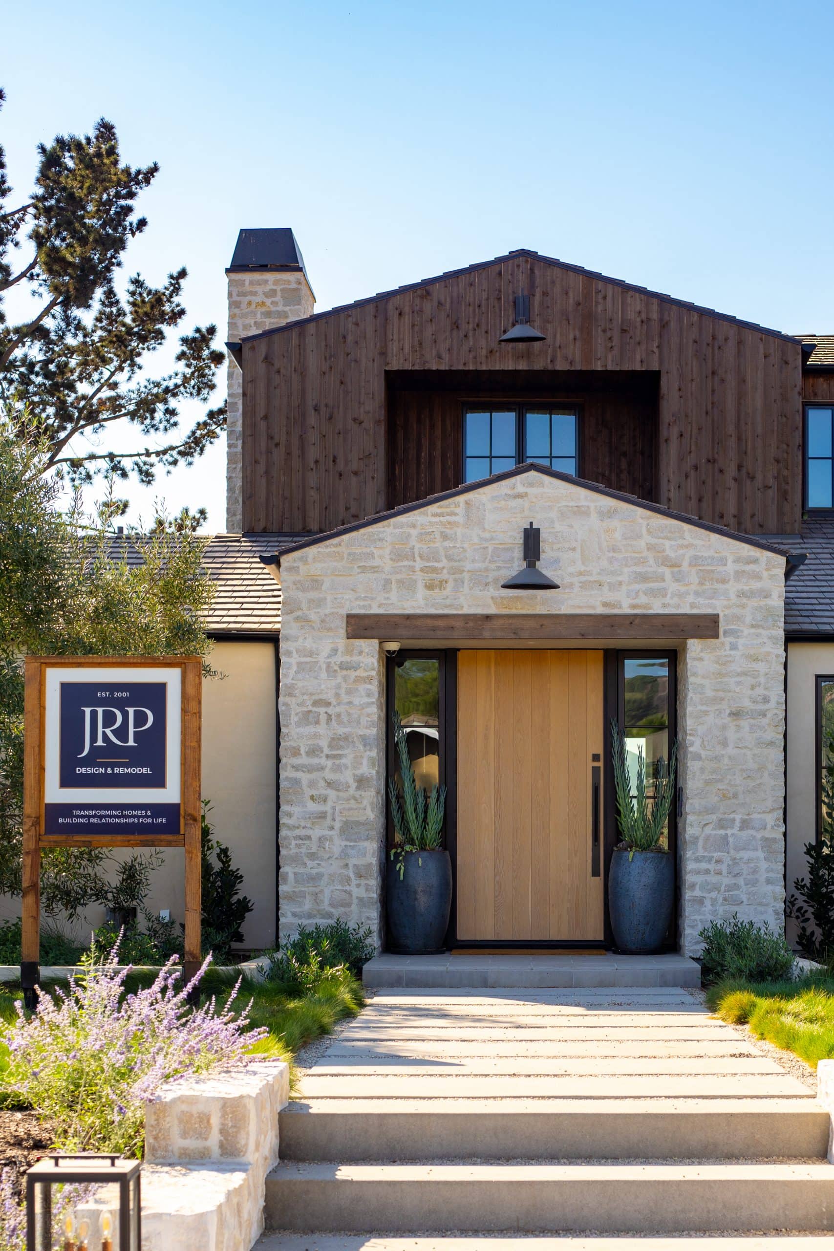 Modern home exterior with stone and wood accents, landscaped entrance, and JRP sign.