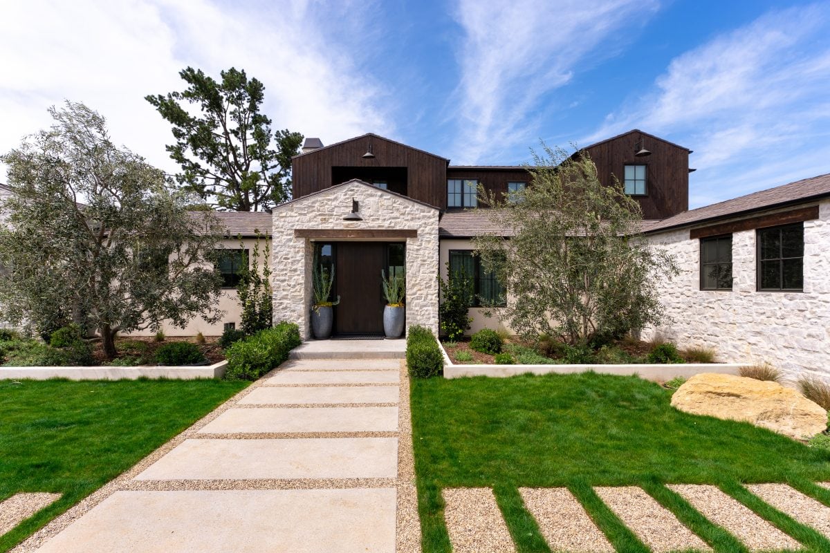 Modern house with stone and wood exterior, landscaped front yard, and pathway.