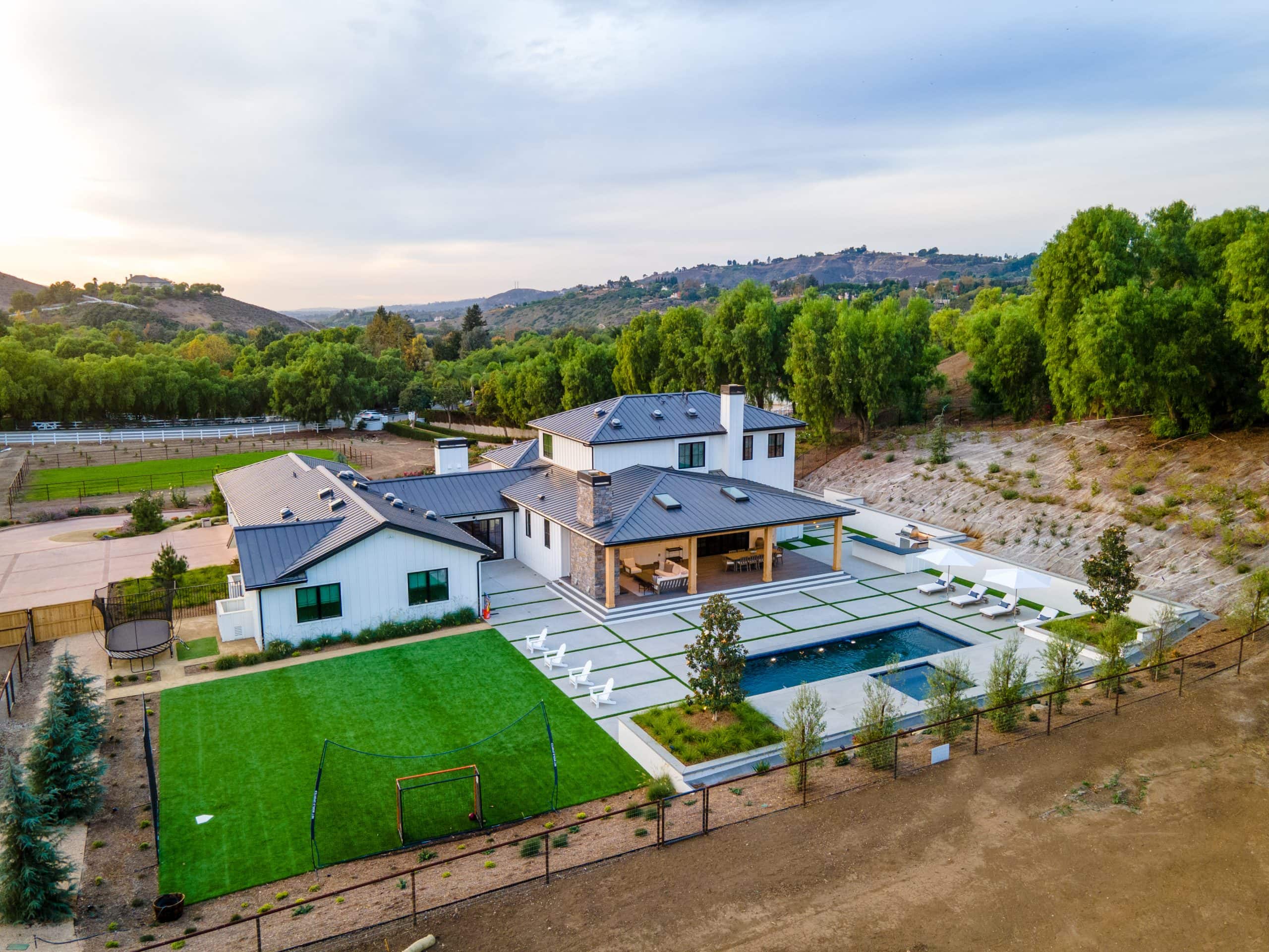 Contemporary farmhouse with pool, lawn, and scenic landscape view.